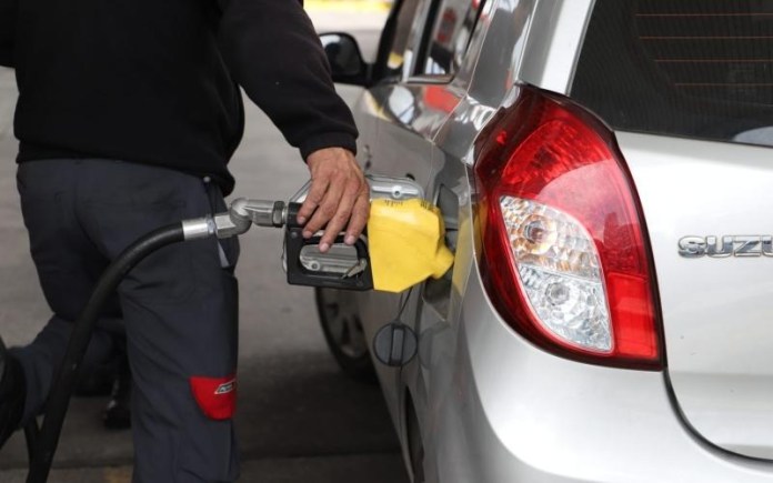 Encargado de gasolinera sirve combustible a un vehículo marcado por el aumento de precios.