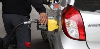Encargado de gasolinera sirve combustible a un vehículo marcado por el aumento de precios.